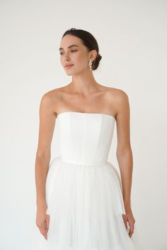 a woman is wearing a white dress and standing in front of a white wall with her hands on her hips