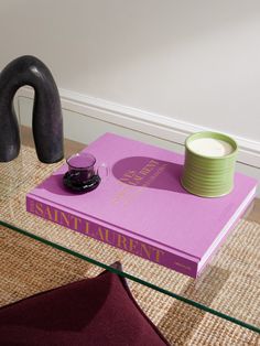 a pink book sitting on top of a glass table next to a vase and chair