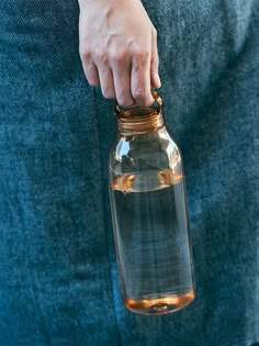 a person holding a glass bottle with water in it