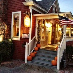 an american flag is on the porch of a house with pumpkins in front of it