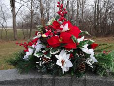 a red and white flower arrangement sitting on top of a stone wall next to trees