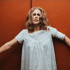 a woman standing in front of a red wall with her arms stretched out to the side