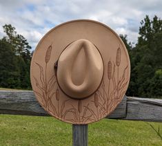 This hand burnt cattail wide brim fedora will add a charming country feel to your wardrobe. The tan material burns brown allowing the intricately burnt and shaded cattails to stand out on this nature inspired hat. The design is original and completely free-handed. For a finishing touch the hat is adorned with a warm brown faux leather hatband. This hat comes carefully packaged in a box. Each of my hats comes beautifully wrapped like a gift, and includes a note card. I would be happy to write a g Burnt Hats For Women, Felt Burning, Custom Cowgirl Hats, Burning Hats, Burnt Hat, Western Hats For Women, Hats Cowgirl, Burned Hats, Diy Hats