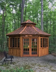 a wooden gazebo in the middle of a wooded area with a bench and chair