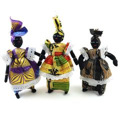 three figurines are standing next to each other on a white surface and one is wearing a colorful dress