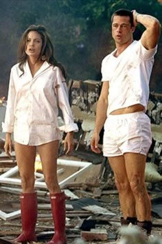 a man and woman standing in front of destroyed buildings with red rubber boots on their feet