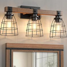 three light fixtures mounted on a wall above a mirror in a bathroom with wood frame and metal cage