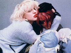 a woman with red hair sitting on the floor kissing another woman's head while they both have their arms around each other