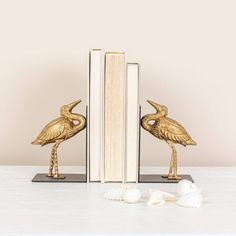 two bookends with birds on them sitting next to an open book and seashells