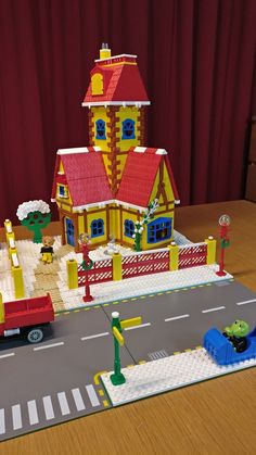 a lego house with cars parked in front of it on a table next to a red curtain