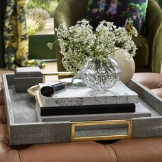 a glass vase with flowers sitting on top of a tray in front of a couch