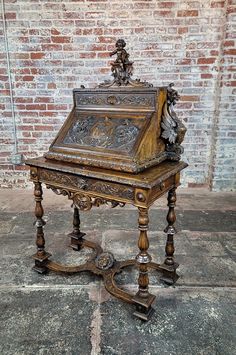 an old wooden desk with carvings on the top and bottom, sitting in front of a brick wall