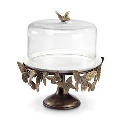 a cake plate with a glass cover and gold butterflies on the bottom, sitting on a metal base