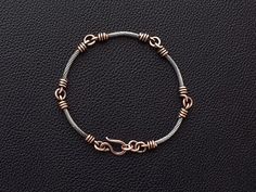 a silver and gold bracelet on a black leather surface with the clasp undone to reveal an interlocked knot