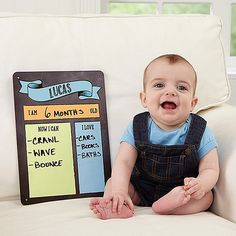 a baby sitting on a couch next to a board with some words written on it