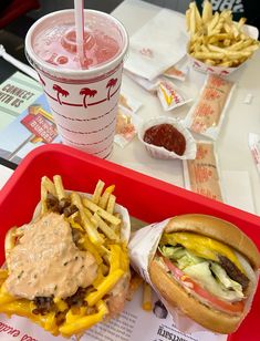 a tray with a burger and fries on it next to a drink in a plastic cup