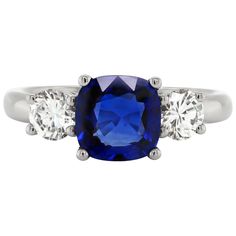 This beautiful engagement ring features a cushion shaped royal blue sapphire weighing a total of 2.19 carats mounted in a four claw, open back setting. The sapphire is accompanied by two round brilliant cut diamonds, one on either side, with a total combined weight of 0.75 carats also in open back, four claw settings, all mounted in platinum. Hallmarked 950, stamped PT950. UK finger size 'O'. Gia Certified Cushion Cut Sapphire Ring In White Gold, Cushion Cut Sapphire Diamond Ring For Formal Occasions, Formal Sapphire Cushion Cut Diamond Ring, Sapphire Platinum Diamond Ring Cushion Cut, Sapphire Cushion Cut Diamond Ring In Platinum, Platinum Sapphire Cushion Cut Diamond Ring, Classic White Gold Sapphire Ring Cushion Cut, Sapphire Diamond Ring With Cushion Brilliant Cut, Sapphire Diamond Ring With Cushion Cut