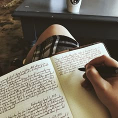 a person writing on an open notebook with a cup of coffee in front of them