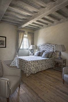 a bed sitting in a bedroom next to two chairs and a lamp on top of a wooden floor