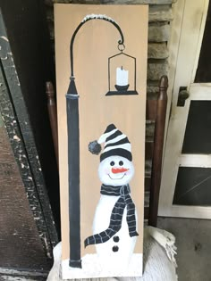 a snowman is standing next to a lamp post with a candle on it and a lantern hanging from the pole