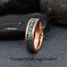 a wedding band with green moss inlays on it, sitting next to some rocks