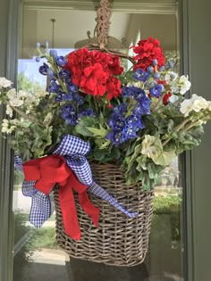 red, white and blue flowers in a basket hanging from the front door with ribbon