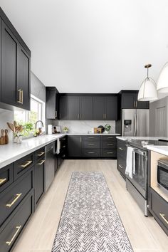 a large kitchen with black cabinets and white counter tops, an area rug on the floor