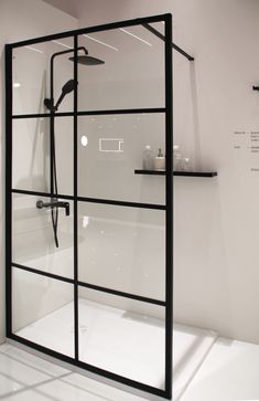 a glass shower door in a bathroom with white walls and flooring, along with black shelves