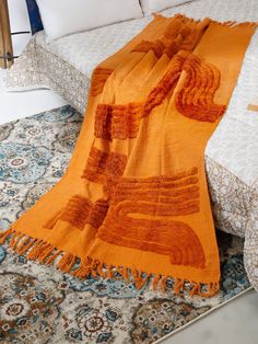 an orange blanket sitting on top of a bed next to pillows and throw rugs