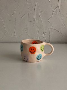 a cup with faces painted on it sitting on top of a white table next to a wall