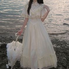 a woman in a white dress is holding an umbrella by the water's edge