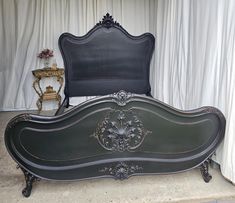 a black bed with an ornate headboard and foot board in front of a white curtained wall