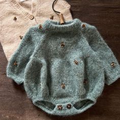 two baby sweaters sitting on top of a wooden floor