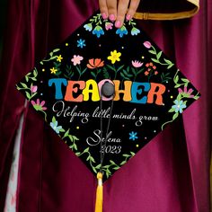 a person wearing a graduation cap with the words teacher written on it and colorful flowers