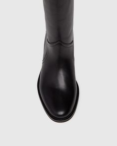 Raina is our take on the classic riding boot. Crafted from a super durable yet luxuriously soft black leather, this timeless straight shaft tall boot is designed with a curved topline that dips at the front and back for a flattering look, western-inspired pattern and stitch detailing, an extended leather welt with tonal stitch details, and a black leather stacked 20mm heel for a slight amount of lift. The classic menswear-inspired details on the outsole include stitching and half toplift for an