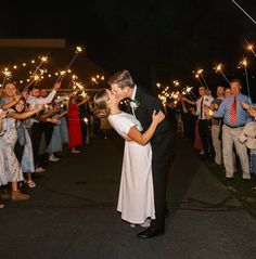 a bride and groom kiss as they hold sparklers in front of their wedding party