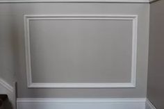 an empty white frame hanging on the wall in a room with stairs and handrails