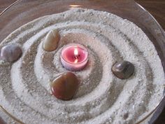 a bowl filled with rocks and a lit candle on top of the sand in it