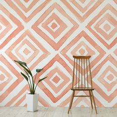 a chair and potted plant in front of a wall painted with an abstract pattern