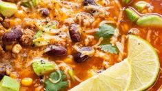 a bowl filled with chili, beans and limes next to a slice of lime