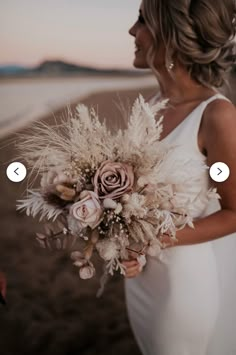 a woman in a white dress holding a flower bouquet on the beach with her face close to the camera