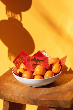 a bowl filled with oranges sitting on top of a wooden table next to a yellow wall