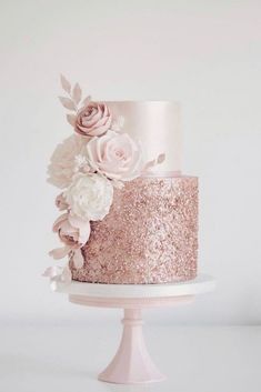 a pink and gold wedding cake with flowers on the top is sitting on a white pedestal