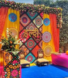 an outdoor area decorated with colorful decorations and flowers on the wall, in front of orange drapes