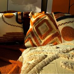 several pillows and blankets on a bed with an orange wall in the backround