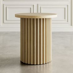 a round wooden table sitting on top of a cement floor next to a white wall