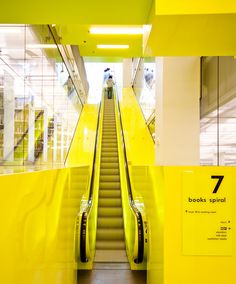 an escalator in a building with yellow walls and stairs leading up to the second floor