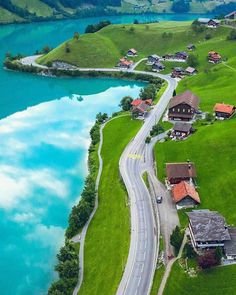 an aerial view of a small village by the water's edge, surrounded by lush green hills