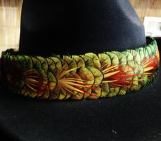 a black hat with a green and red feathered design on it's brim