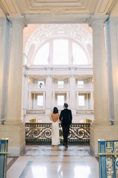 a bride and groom standing in the middle of an ornate building with columns on either side